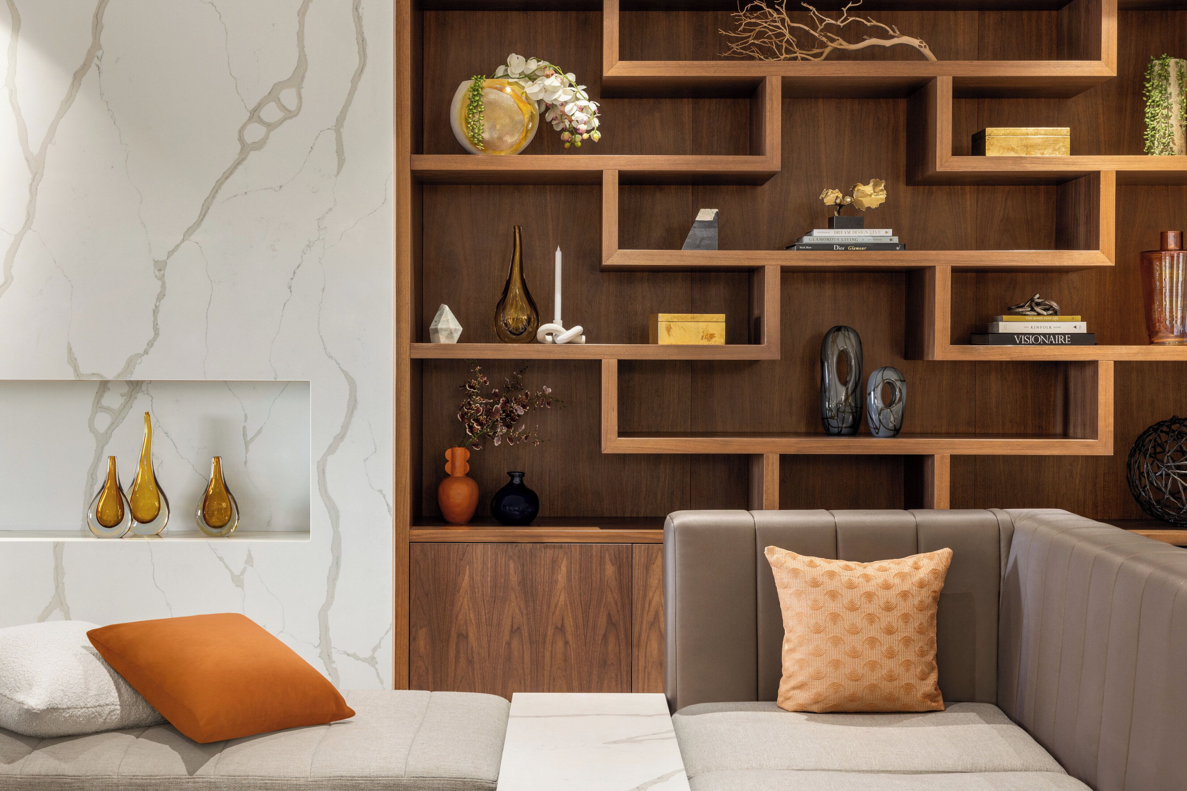 A modern living room with a sectional sofa, a wooden shelving unit, and decorative items.