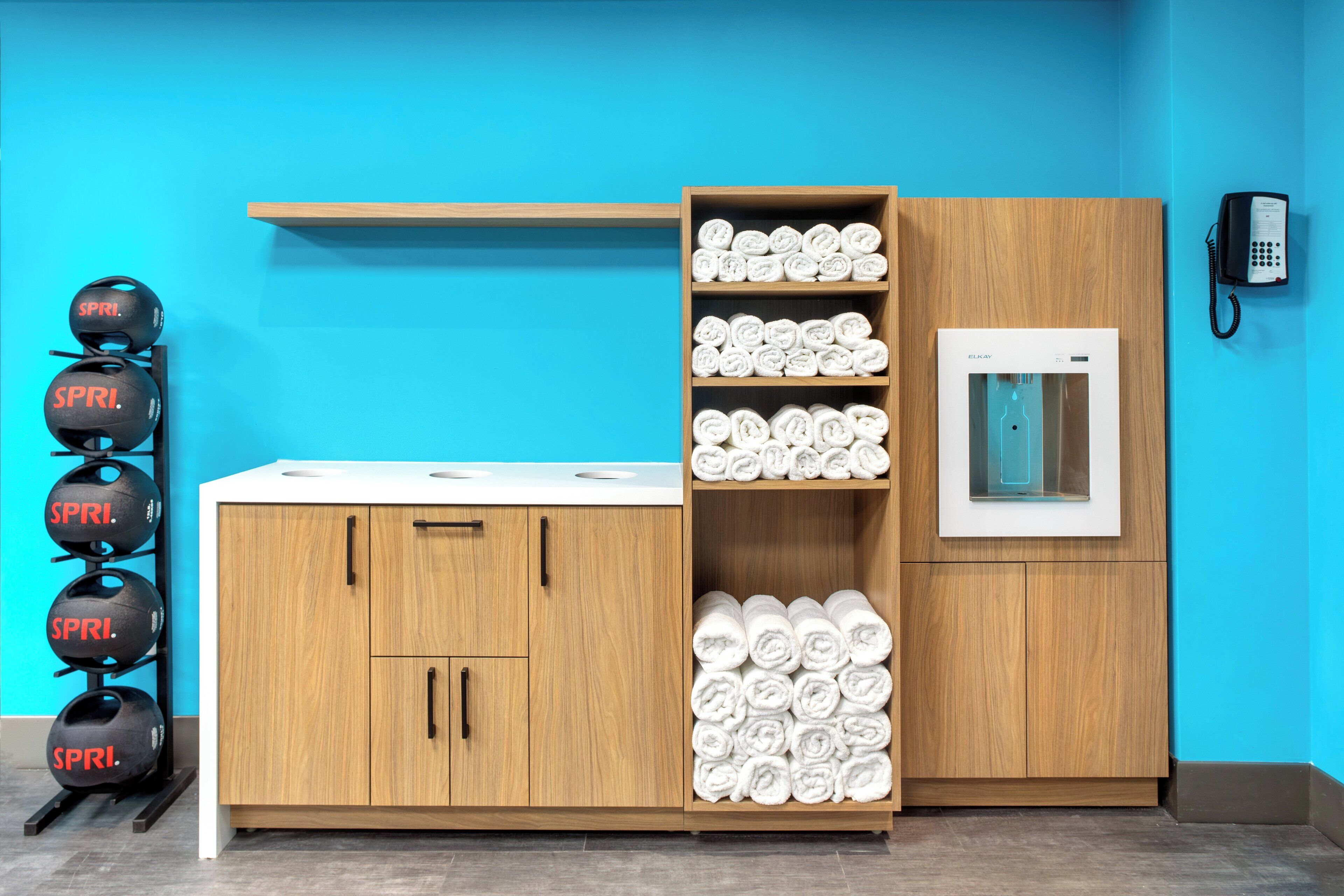 A room with a wooden cabinet, a shelf with rolled towels, a water dispenser, and a phone.