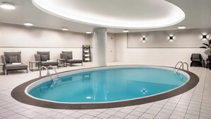 Une piscine intérieure de forme circulaire, entourée de chaises longues et dotée d’un sol carrelé.
