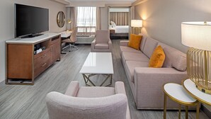 A hotel room with a flat-screen TV, a desk with a chair, a sofa with cushions, a coffee table, and a lamp. - Crowne Plaza Toronto Airport by IHG (Toronto)
