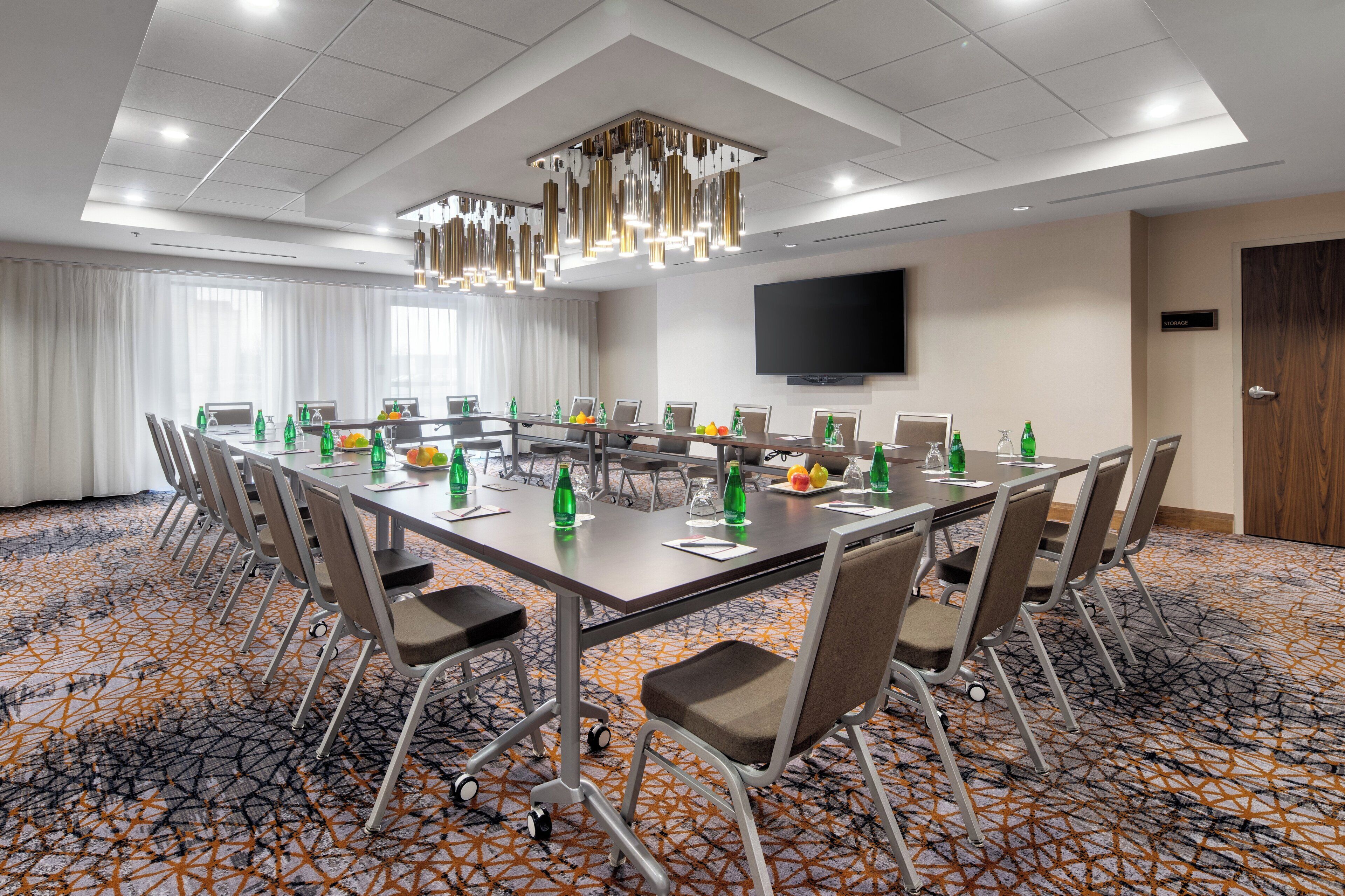A conference room with a long table, chairs, a flat-screen TV, and a storage sign on the wall.