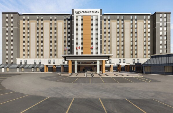 A large hotel building with multiple floors, a central entrance, and a parking lot in front.
