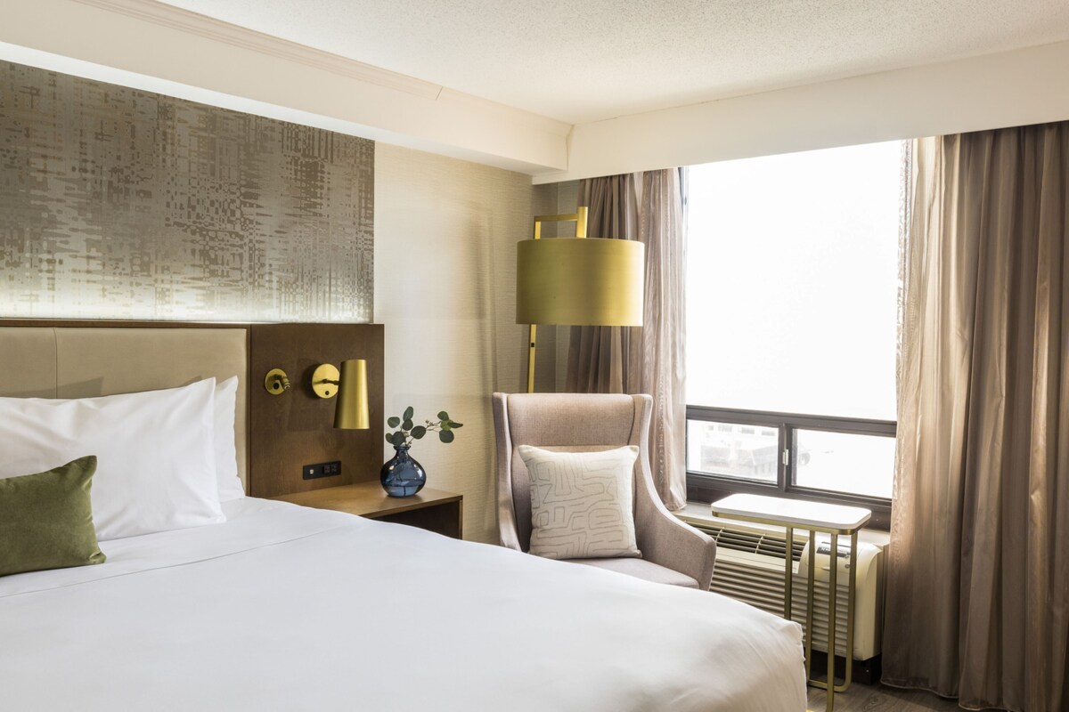 Una habitación de hotel con una cama grande, una silla, un escritorio y una ventana con cortinas.