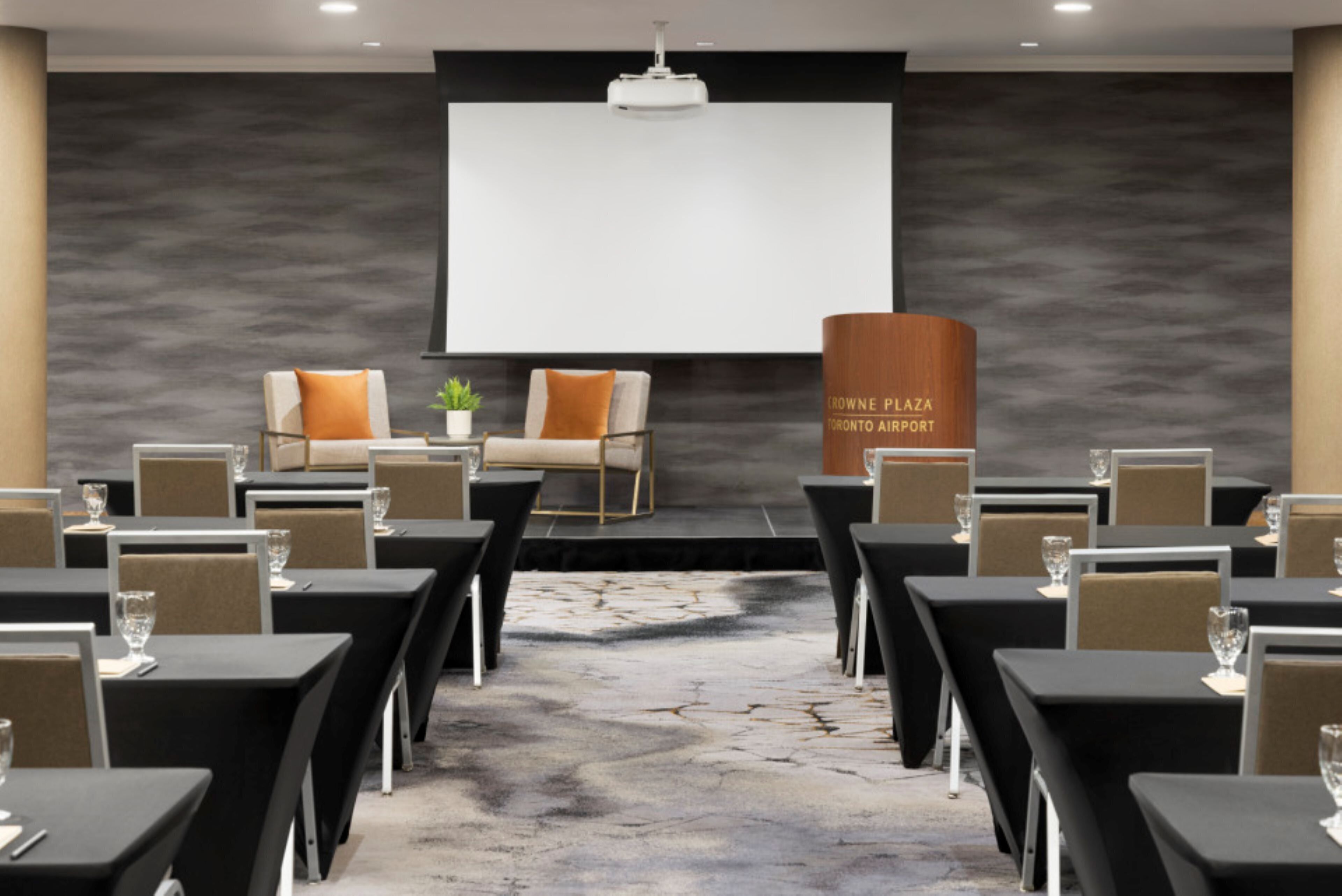 Una sala de conferencias con una pantalla grande, mesas y sillas dispuestas para una reunión.