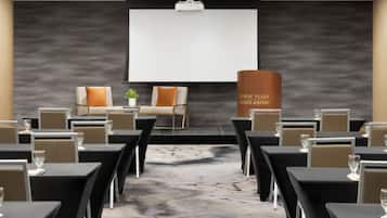 Una sala de conferencias con una pantalla grande, mesas y sillas dispuestas para una reunión.