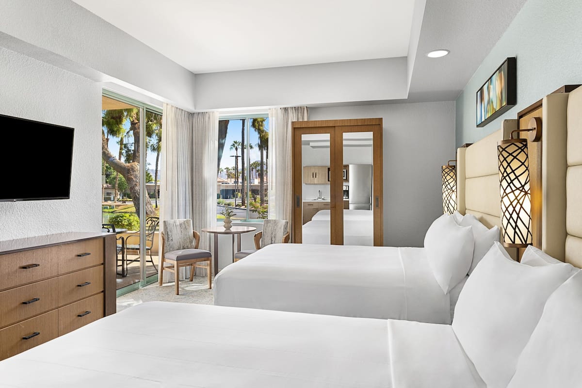 Habitación de hotel con dos camas, televisión, escritorio y vistas al exterior.