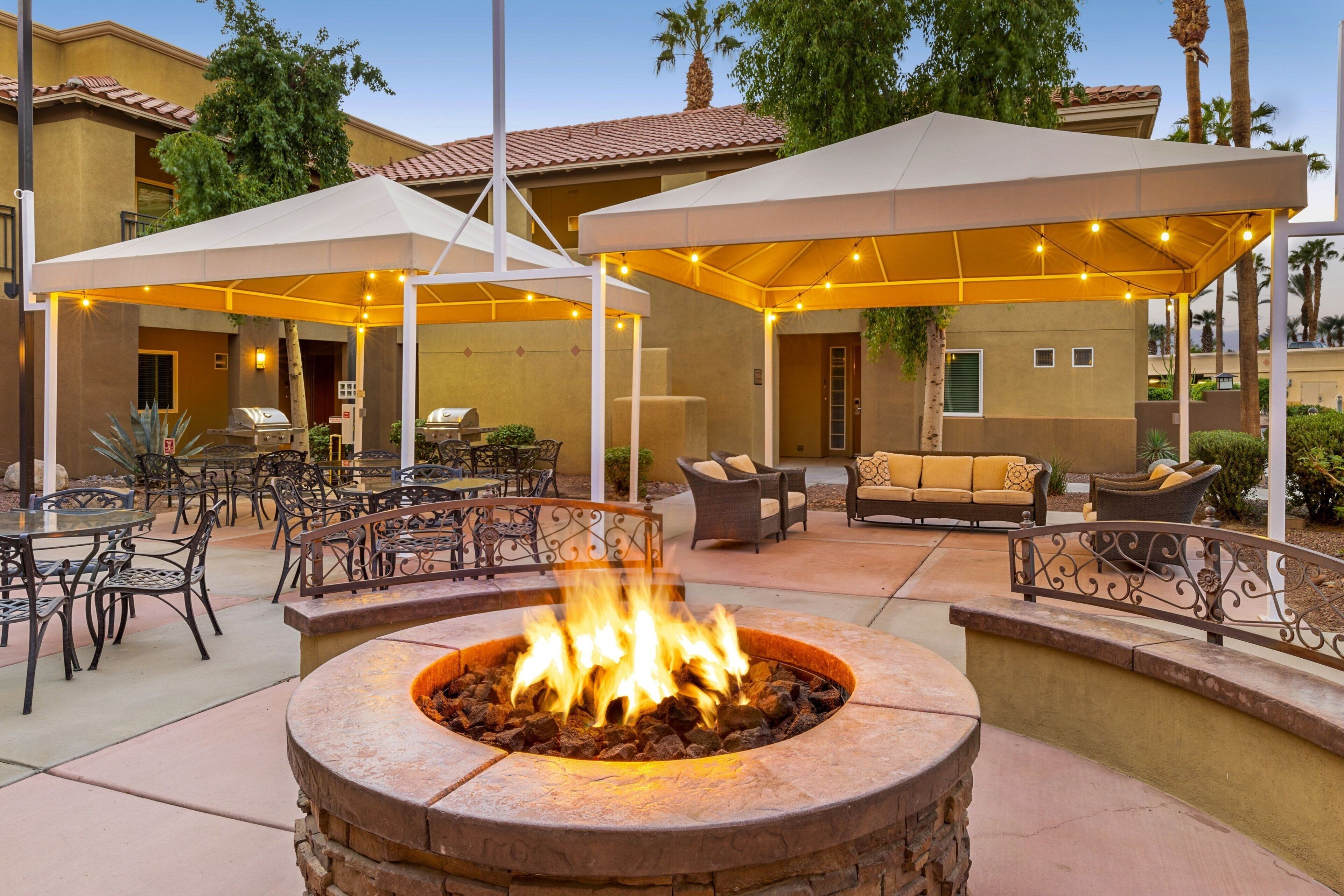 An outdoor patio area with a fire pit, covered seating, and dining tables.