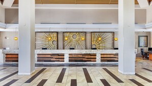 Een ruime lobby met een receptiebalie, modern interieur en een hoge plafond.