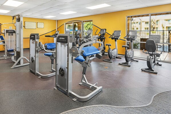 Een sportschool met cardioapparatuur, krachttrainingsapparatuur en een blauwe bank.