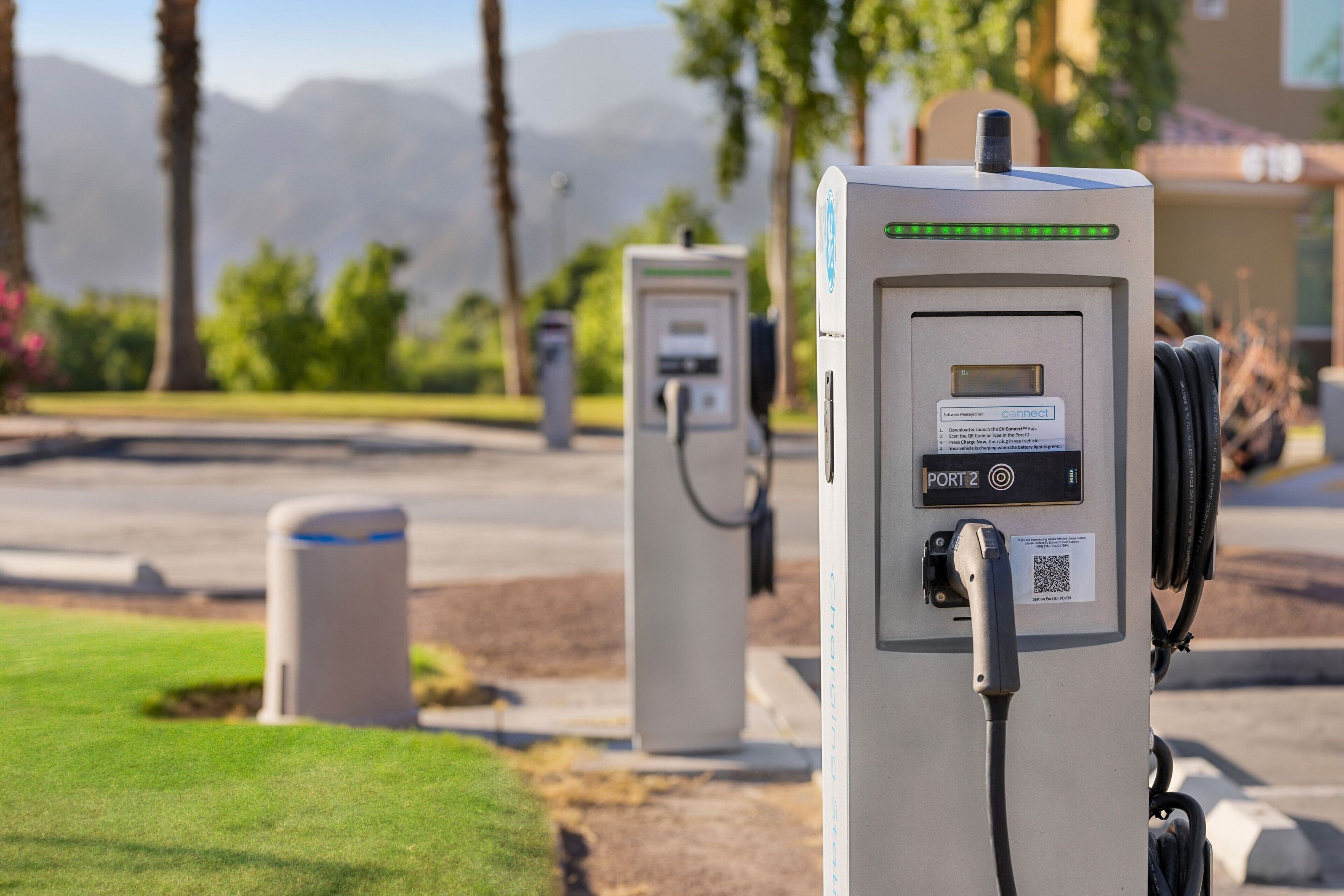 Electric vehicle charging stations with a clear view of the surrounding area, including a road, trees, and a building in the background.