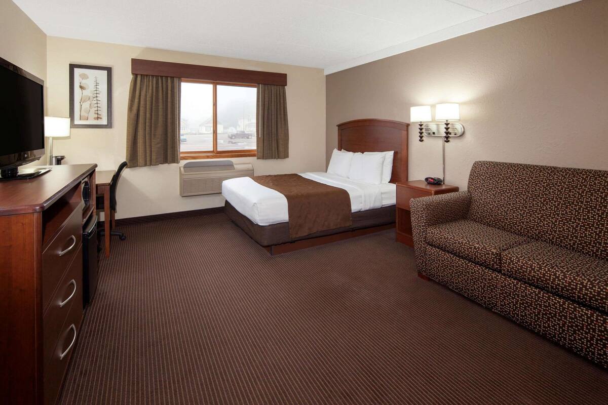 Ein Hotelzimmer mit einem Bett, einem Schreibtisch, einem Fernseher, einer Couch und einem Vorhangfenster.