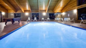 Une piscine intérieure dotée d’un plafond en bois et de murs carrelés, entourée de chaises longues et d’une table de billard.