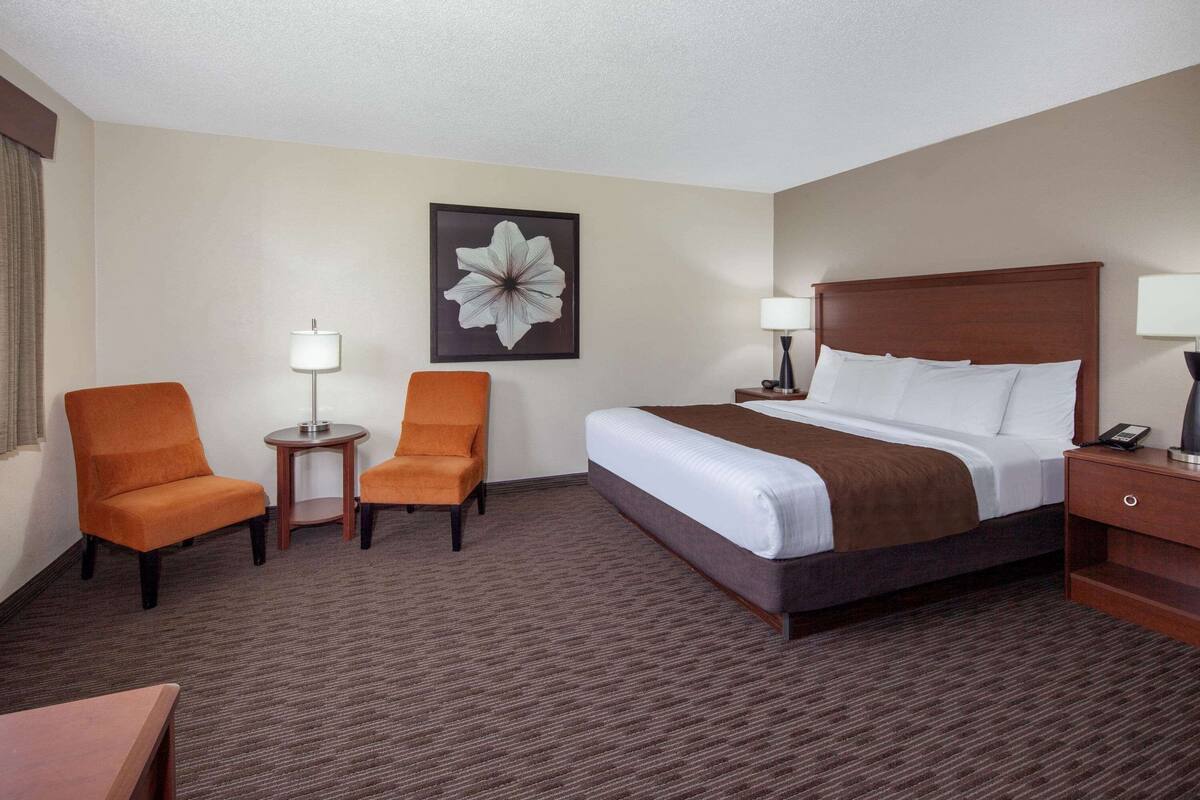 Ein Hotelzimmer mit einem großen Bett, zwei Sesseln, einem kleinen Tisch und einem Blumenbild an der Wand.