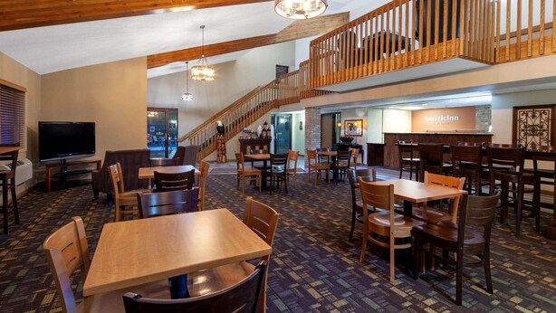 Un hall d’hôtel avec plusieurs tables et chaises en bois, un escalier et une enseigne indiquant « AmericInn ».