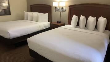 Two twin beds with white linens, a nightstand with a clock, and a wall-mounted lamp.