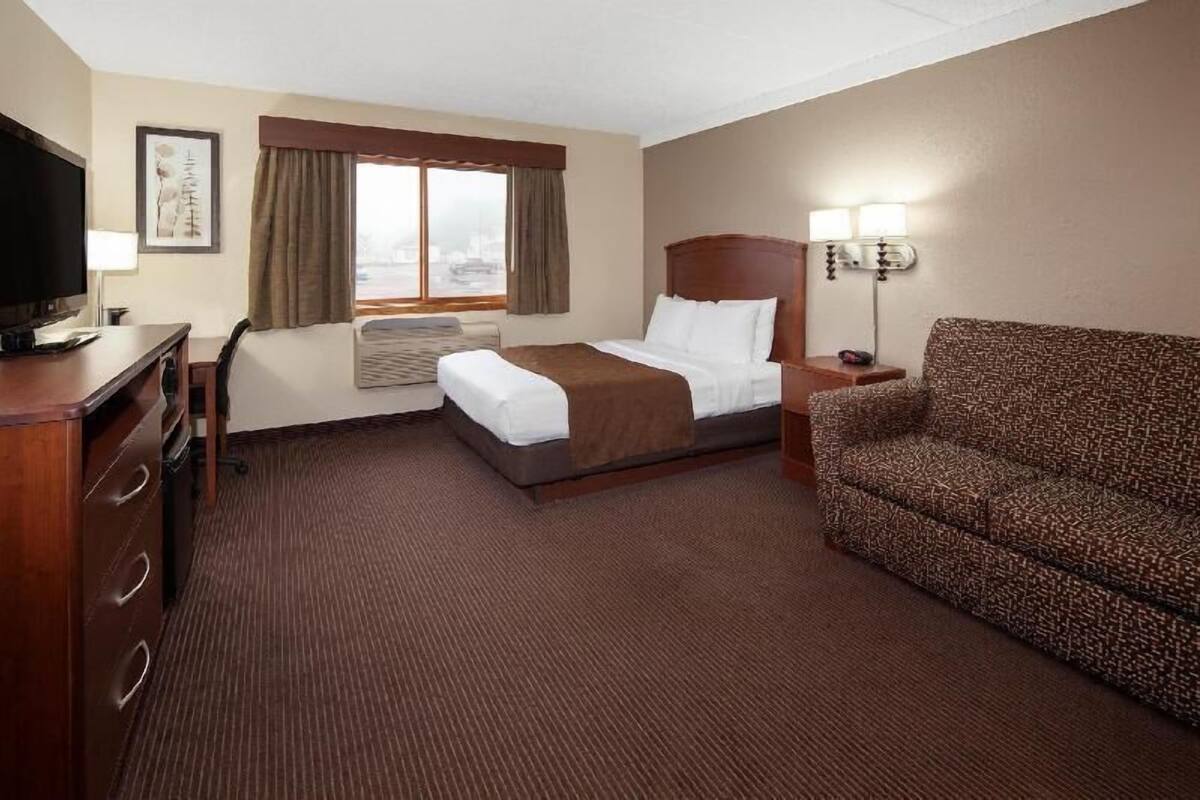 Ein Hotelzimmer mit einem Bett, einem Schreibtisch, einem Fernseher, einem Sofa und einem Fenster mit Vorhängen.