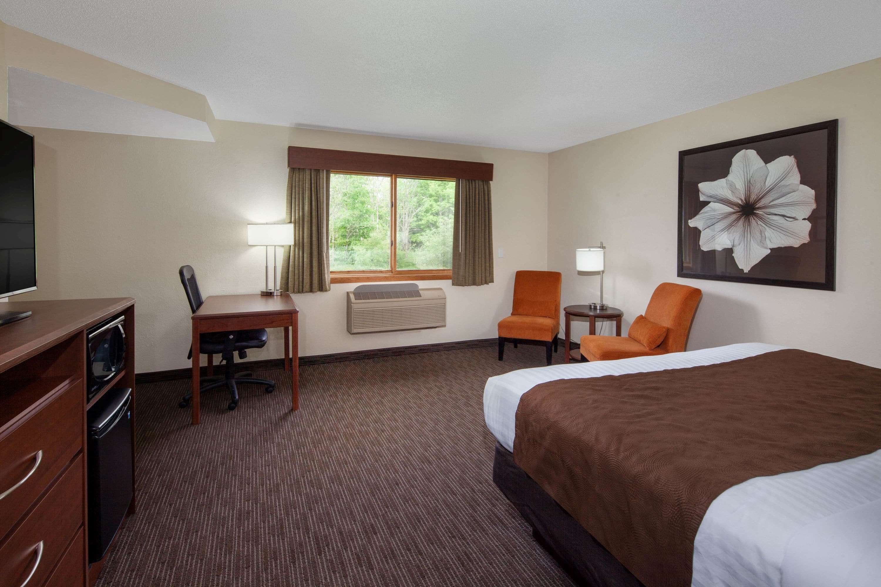 A hotel room with a bed, desk, chair, TV, and air conditioning unit.