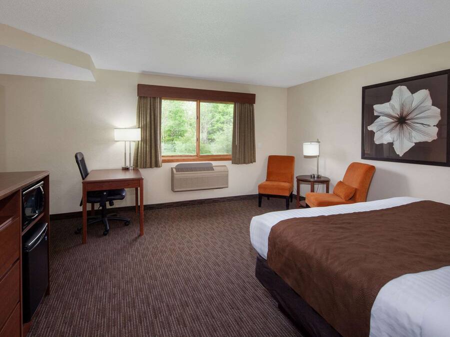 A hotel room with a bed, desk, chair, TV, and air conditioning unit.