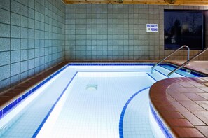 A swimming pool with a capacity sign, tiled walls, and a window with a view.
