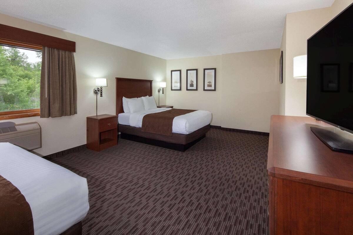 Ein Hotelzimmer mit zwei Betten, einem Schreibtisch, einem Fernseher und gerahmten Bildern an der Wand.
