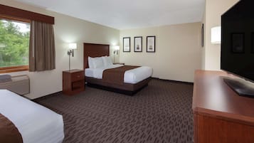 A hotel room with two beds, a desk, a television, and framed pictures on the wall.