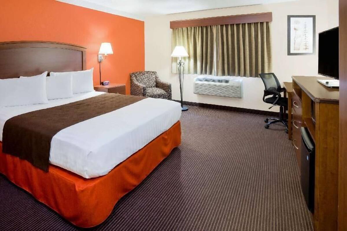 Ein Hotelzimmer mit Bett, Schreibtisch, Stuhl, Lampe und Fernseher.