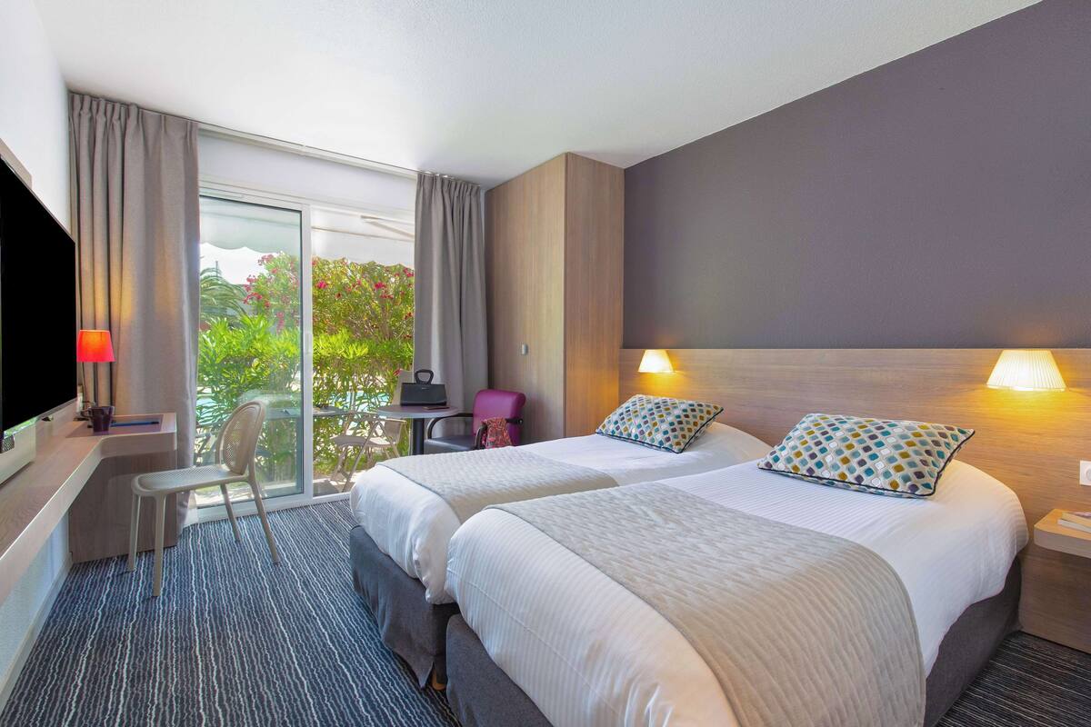 Een hotelkamer met twee bedden, een bureau, een stoel en een televisie.