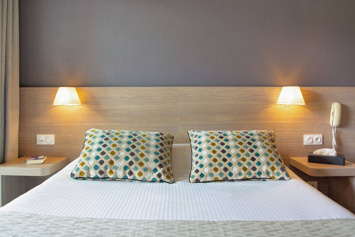 Hotelkamer met een groot bed, twee nachtkastjes, een telefoon en twee wandlampen.