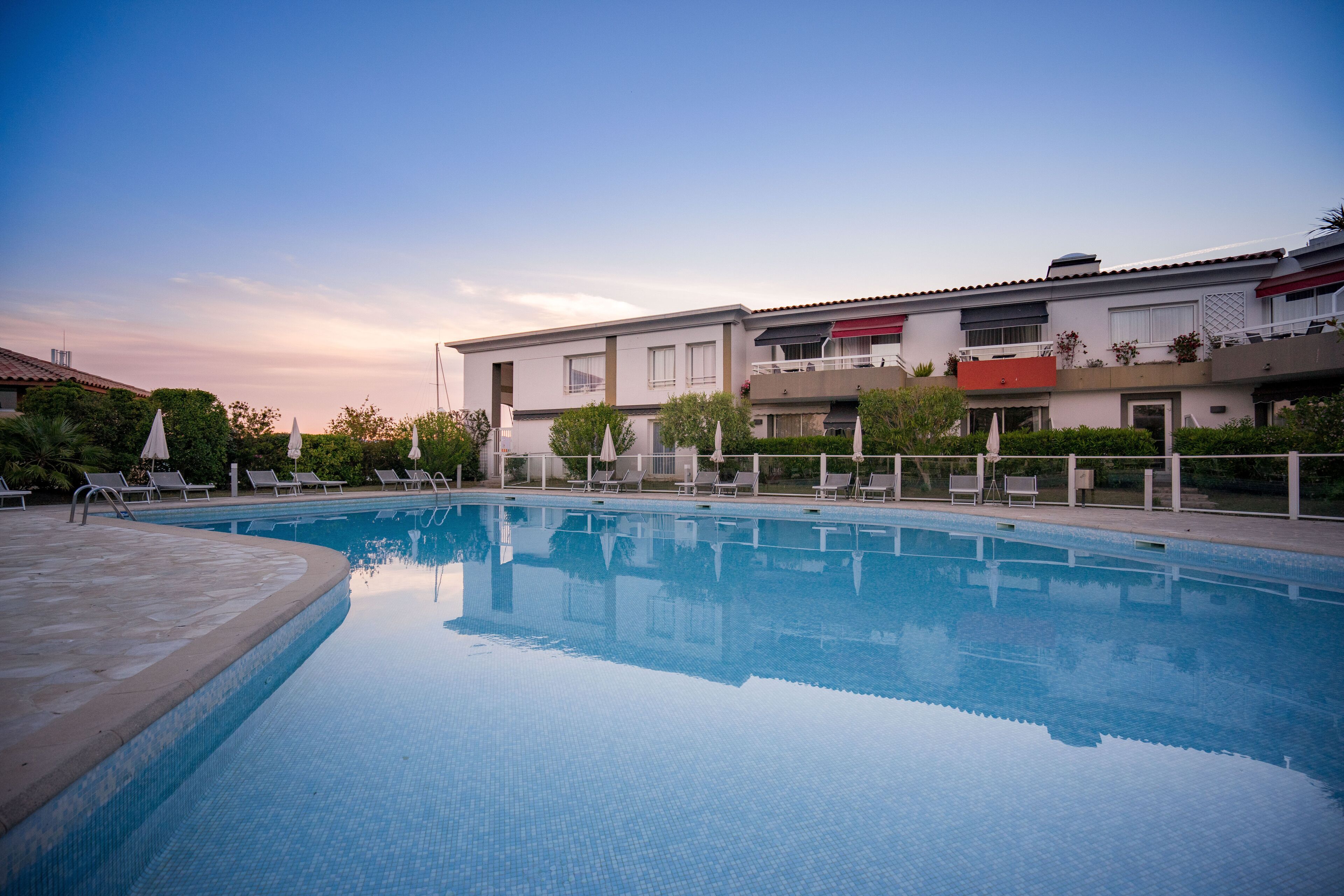 A swimming pool with lounge chairs and a building with balconies in the background.
