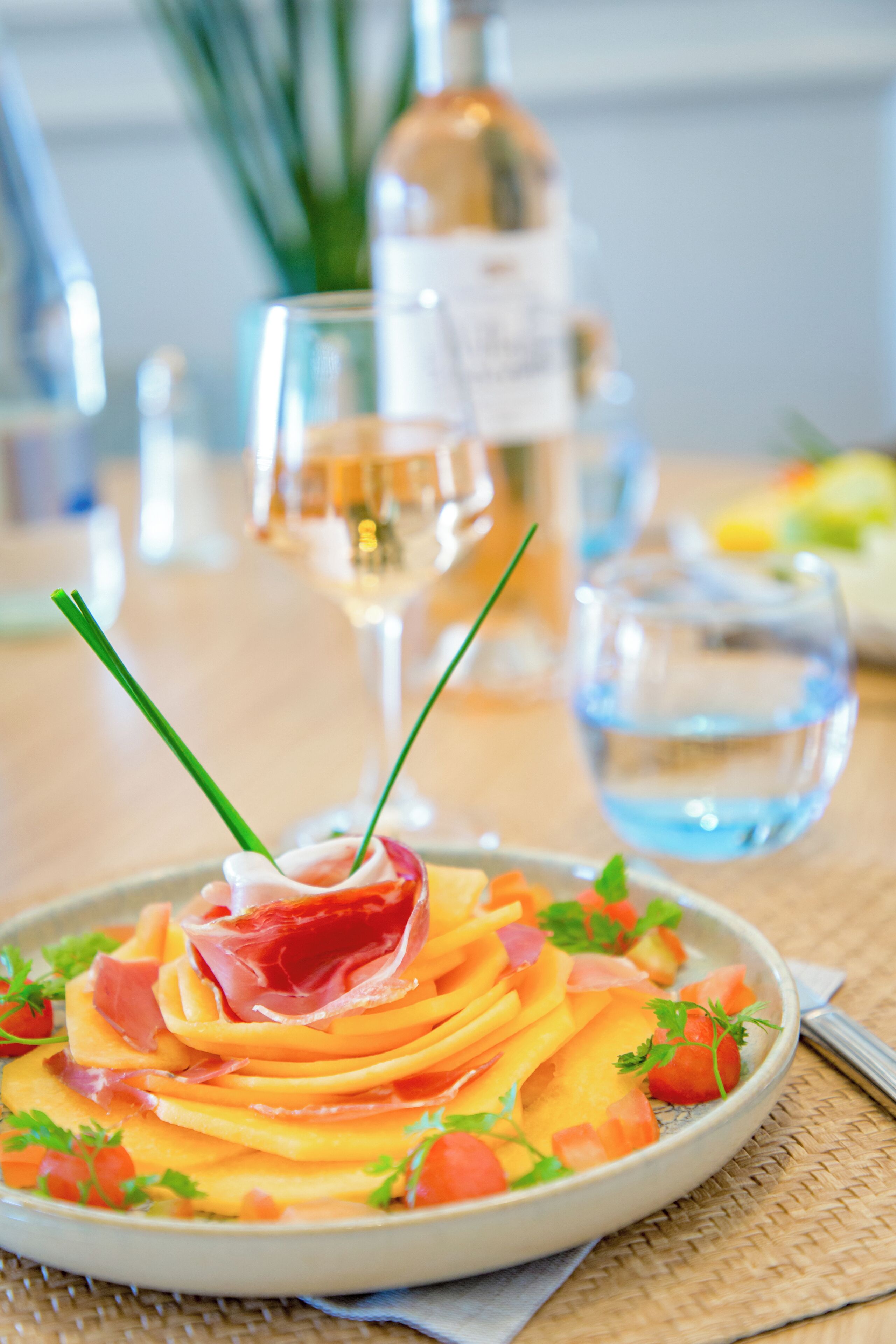 A plate of food with a garnish of green chives, a glass of water, and a bottle in the background.