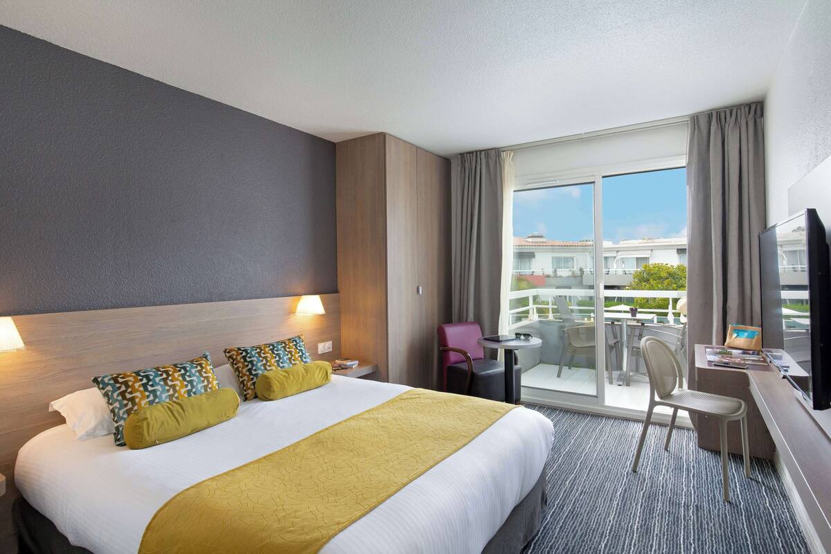 Een hotelkamer met een groot bed, een bureau, een stoel en een balkon met uitzicht.