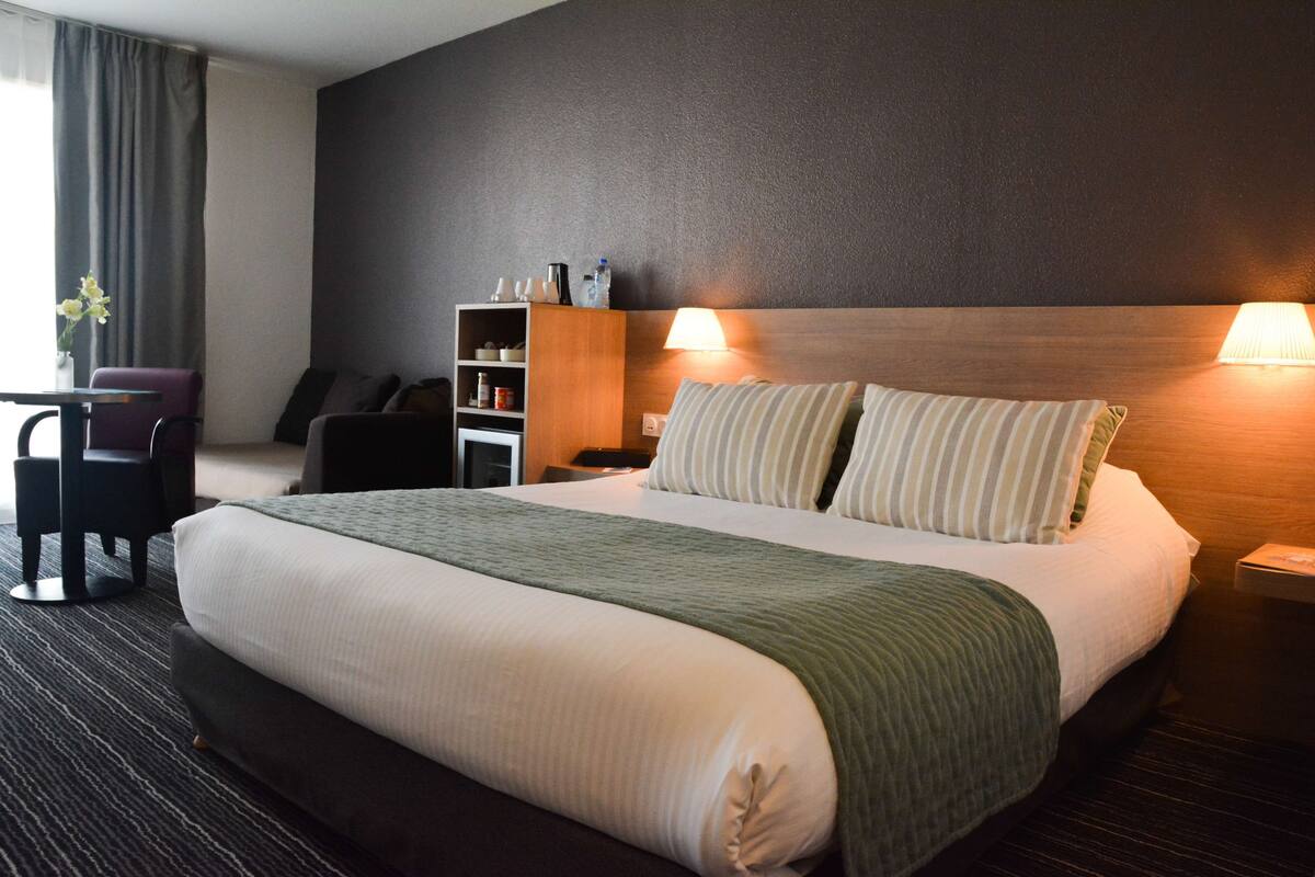 Een hotelkamer met een groot bed, twee bedlampen, een nachtkastje, een bureau met een stoel en een klein boekenrek.