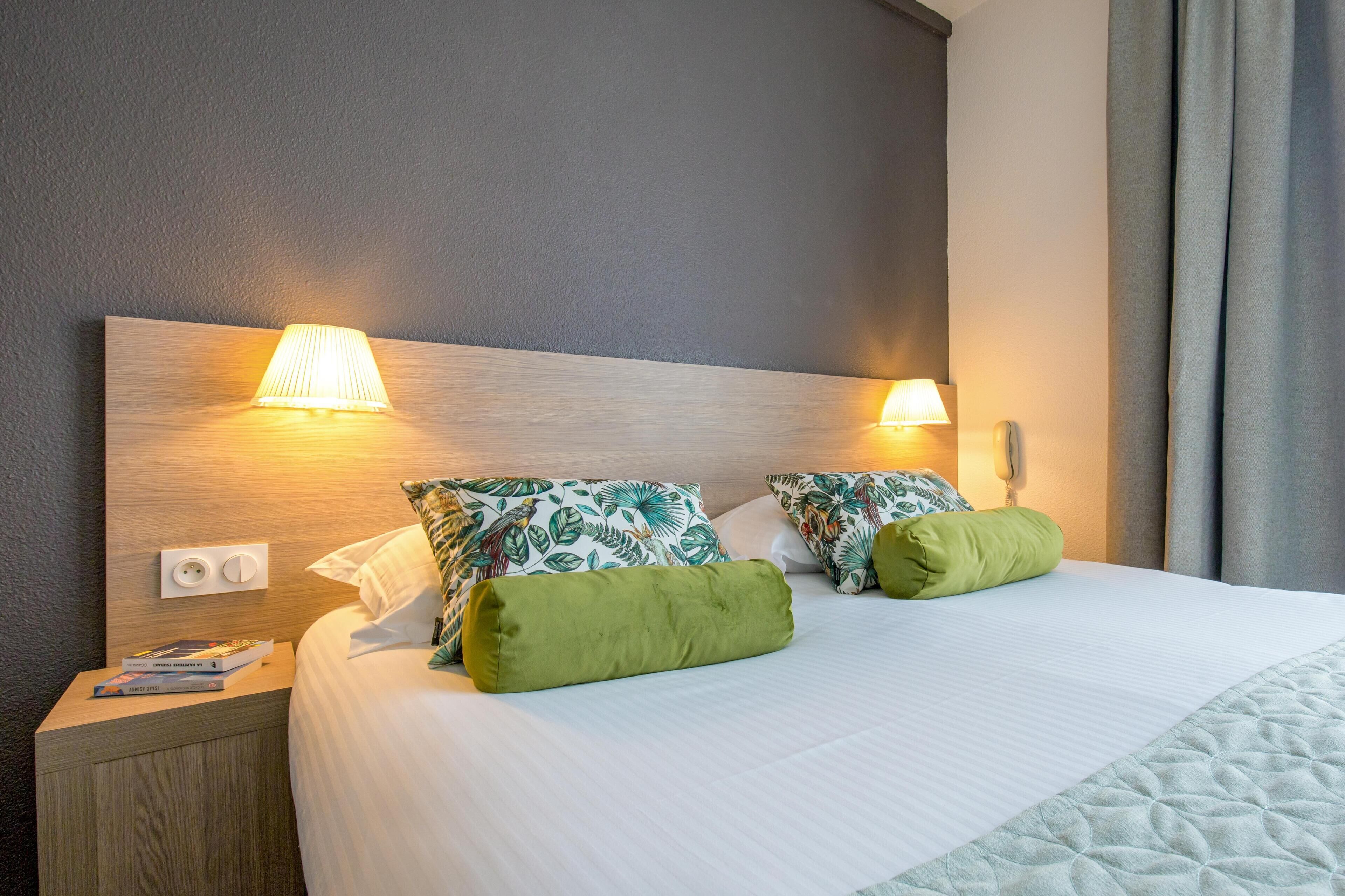 A neatly made bed with green pillows, a wooden headboard, and two wall-mounted lamps.
