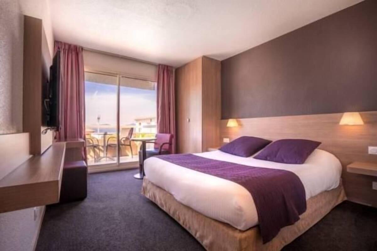 Hotelkamer met een bed, bureau, stoel, televisie en een balkon met uitzicht.