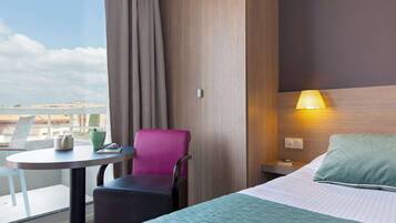 Habitación de hotel con cama, una mesa con silla, una lámpara y vistas a la ciudad.