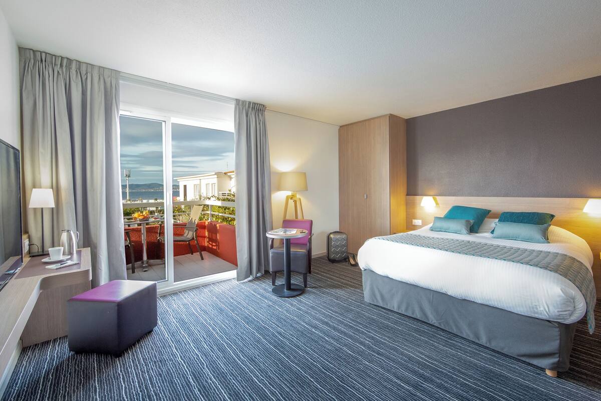 Een hotelkamer met een groot bed, een bureau, een stoel en uitzicht op de stad.