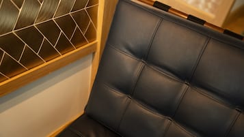 A corner of a room with a dark leather chair and a wooden-framed window with a geometric pattern.
