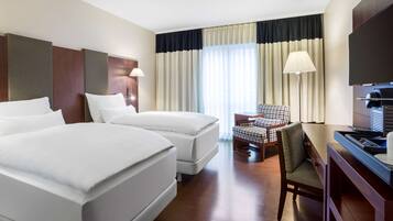 A hotel room with two beds, a desk, a chair, a TV, and a large window with curtains.