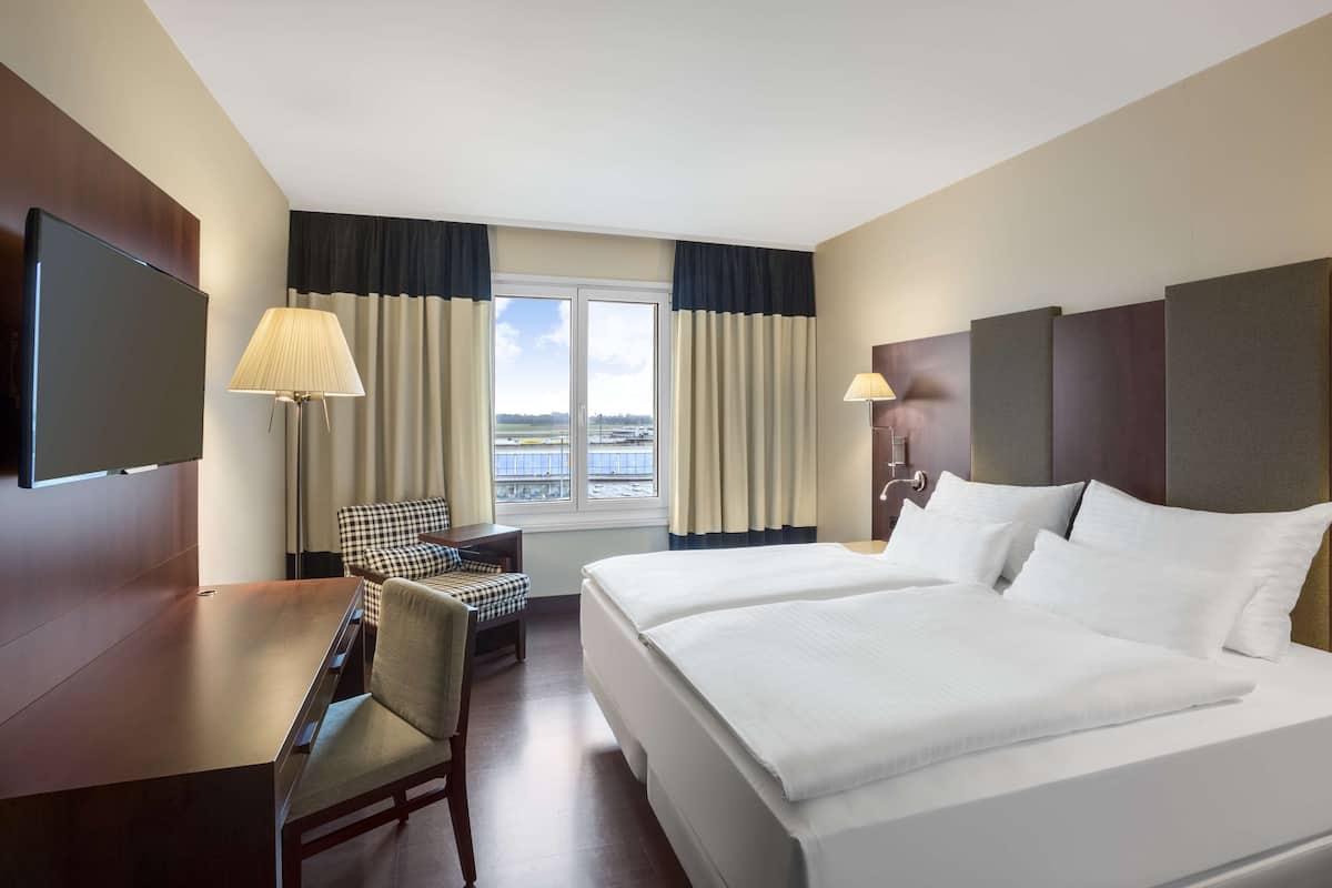 Une chambre d’hôtel avec un grand lit, un bureau, une chaise, une télévision et une fenêtre avec des rideaux.
