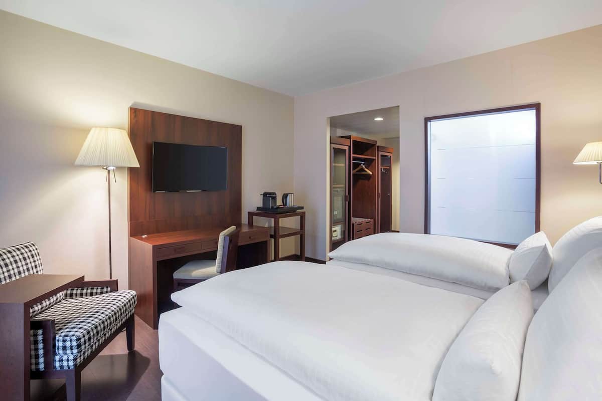 Une chambre d’hôtel comprenant un lit, un bureau avec une chaise, un téléviseur fixé au mur, une armoire et une lampe.