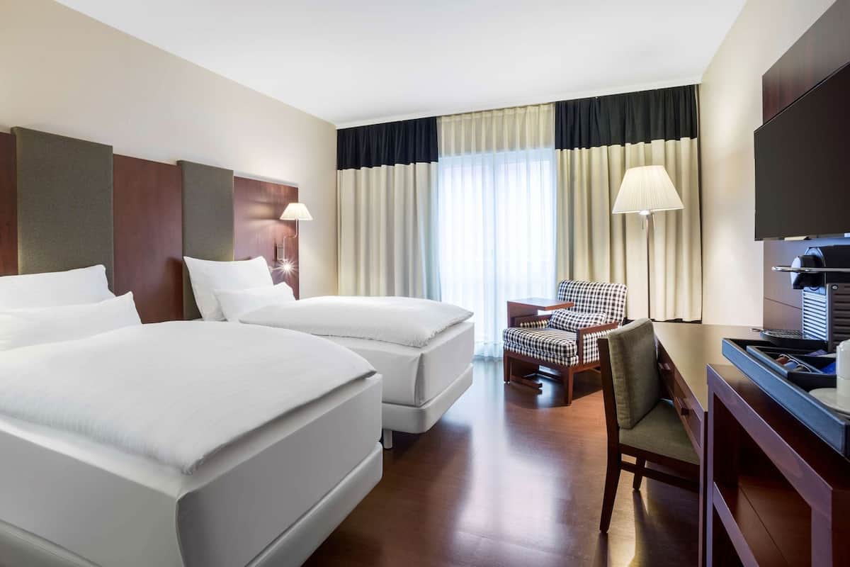 Une chambre d’hôtel avec deux lits, un bureau équipé d’une machine à café, une chaise et un téléviseur.