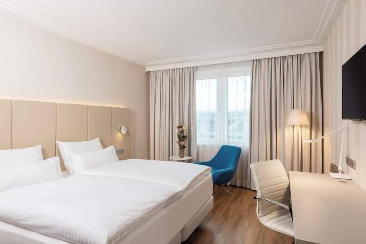 Une chambre d’hôtel avec un grand lit, un bureau, une chaise, une télévision et une fenêtre avec des rideaux.