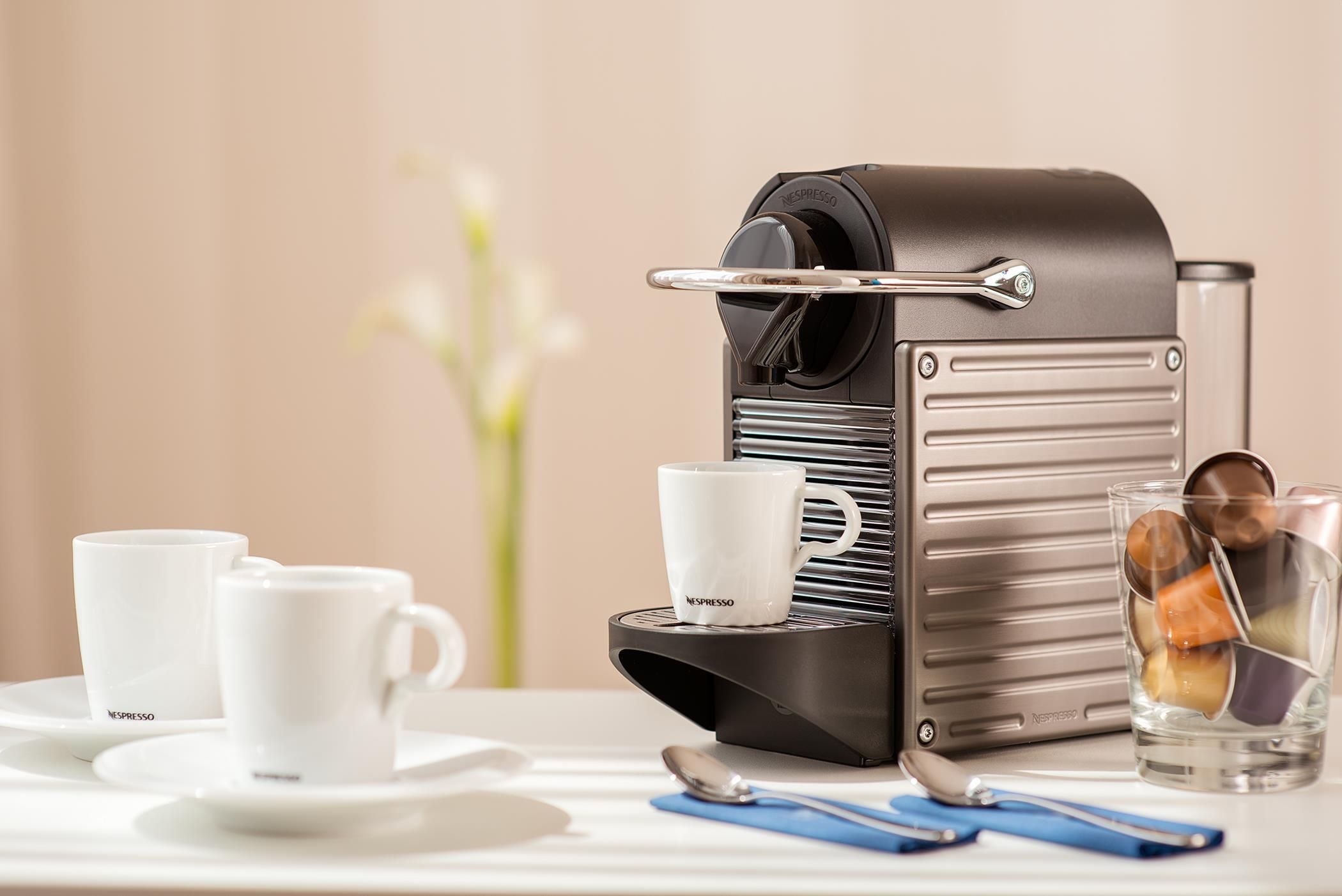 Una máquina de café Nespresso con dos tazas y un vaso de café sobre una mesa.