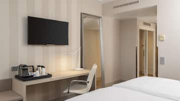 Una habitación de hotel con cama, escritorio, cafetera y tazas, televisor y espejo.