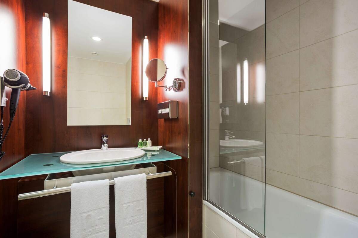 Une salle de bain avec un lavabo à vasque en verre, un miroir, un sèche-cheveux et une cabine de douche en verre.