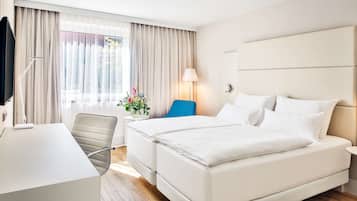 Ein Hotelzimmer mit Bett, Schreibtisch, Stuhl und einem fensterbepflanzten Fenster.