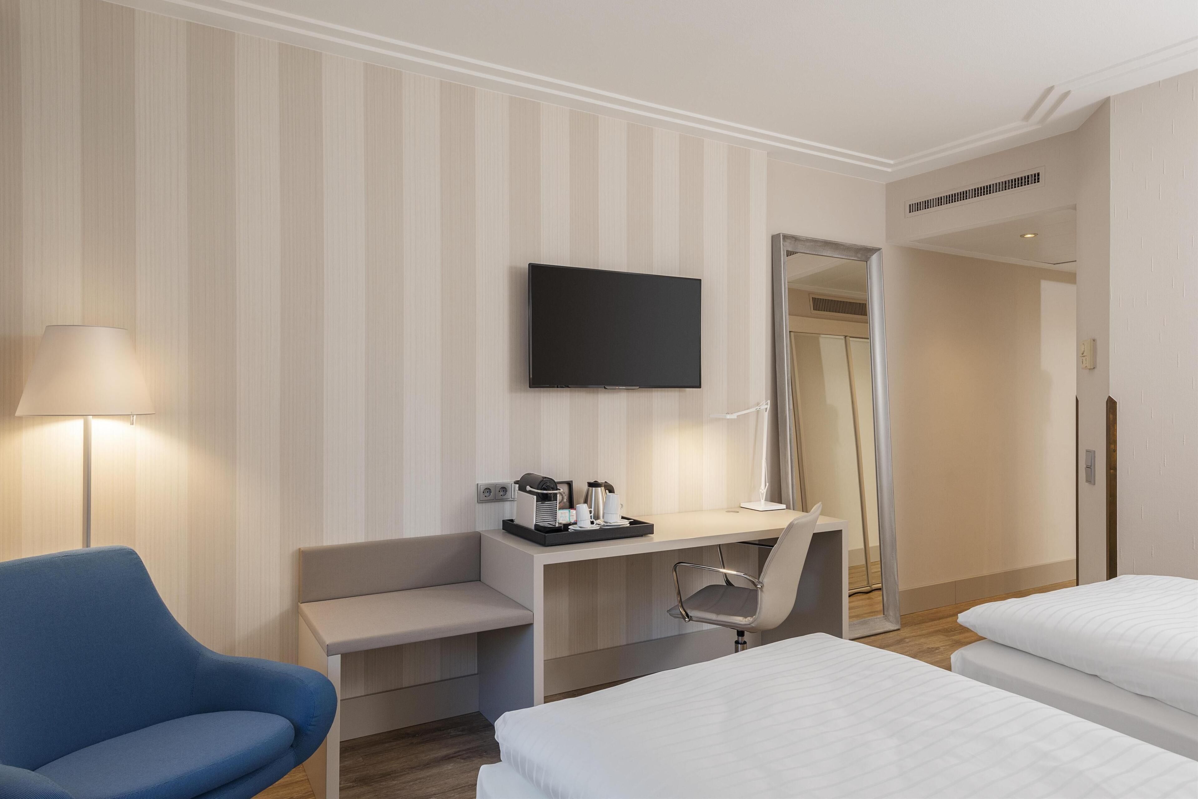 Una camera d'albergo con un letto, una scrivania con una sedia, una TV e una lampada.