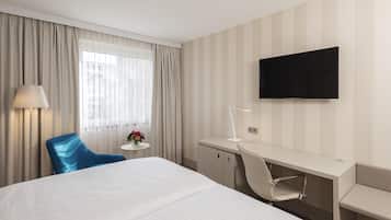 Ein Hotelzimmer mit einem großen Bett, einem Schreibtisch, einem Sessel, einem Fernseher und einem Fenster mit Vorhängen.