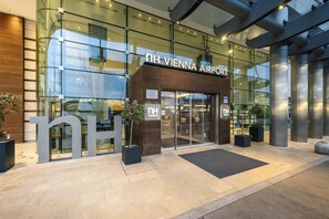 The exterior of the NH Vienna Airport Hotel with a glass facade, large signage, and a modern entrance.