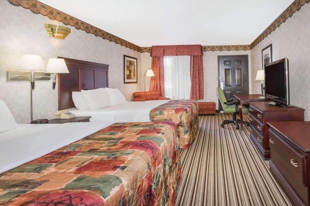 Ett hotellrum med två sängar, ett skrivbord, en tv och ett fönster med gardiner.